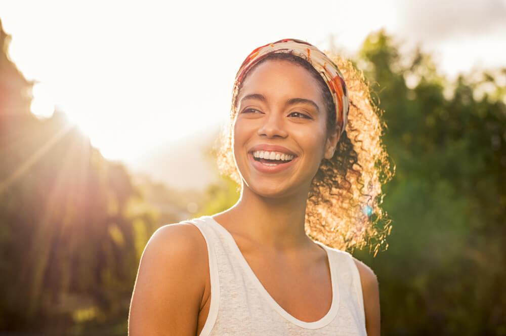 Woman smiling with the sun shining behind her.
